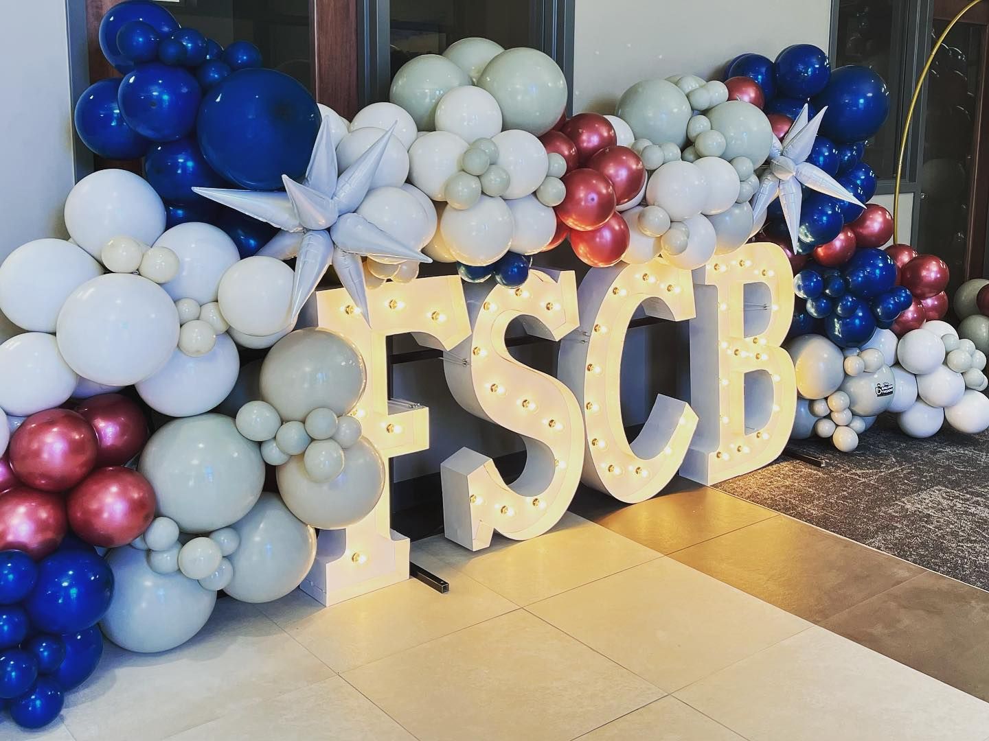 Blue, white, and pink balloon display with large gold “ESCB” letters at an indoor entrance.