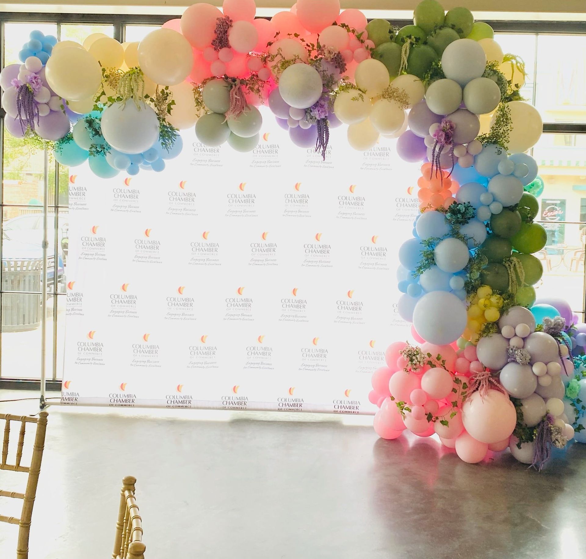 Pastel balloon arch framing a white event backdrop in a bright indoor venue