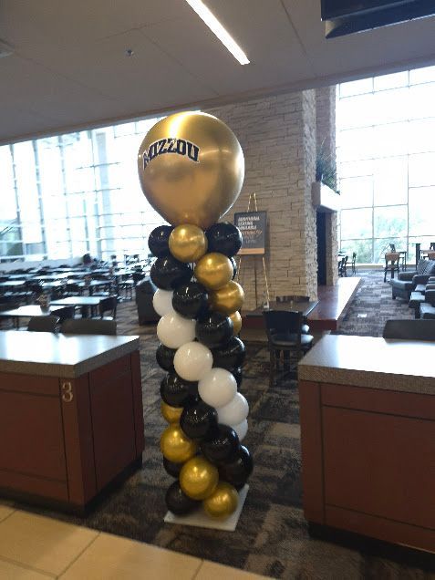 Gold, white, and black balloon column in a lobby beside wooden counters and large windows