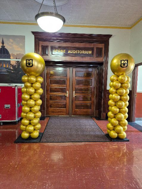 Entrance to a lecture auditorium with gold balloon columns and double wooden doors