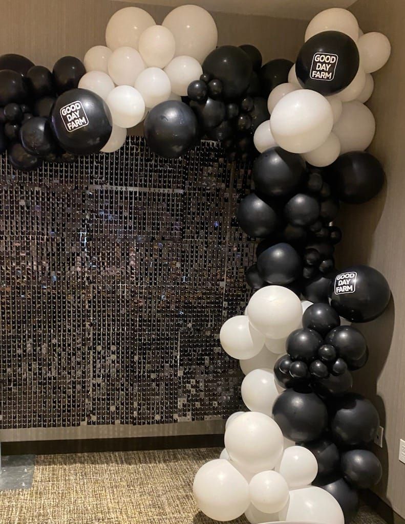 Black, white, and silver balloon arch framing a woven backdrop indoors