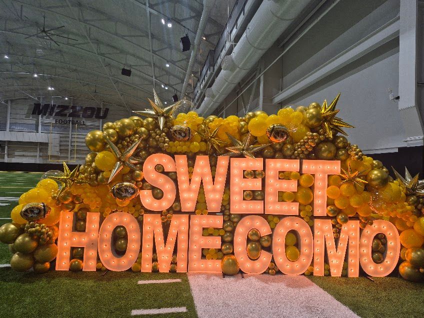 Orange balloon display reading “SWEET HOMECOMO” in a decorated indoor venue