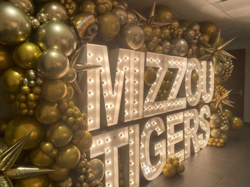 MIZZOU TIGERS marquee sign with gold balloons and star decorations on a stage-like floor