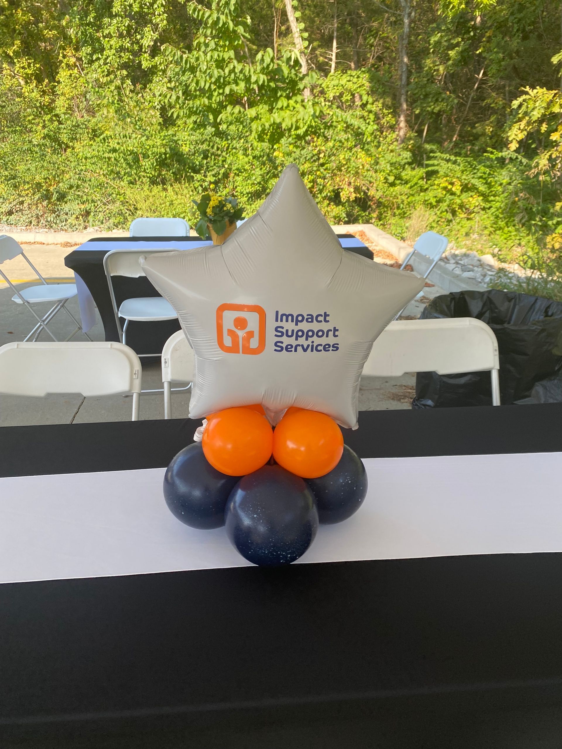 Decorative balloon centerpiece with a white star balloon and orange and blue balloons on a table outdoors