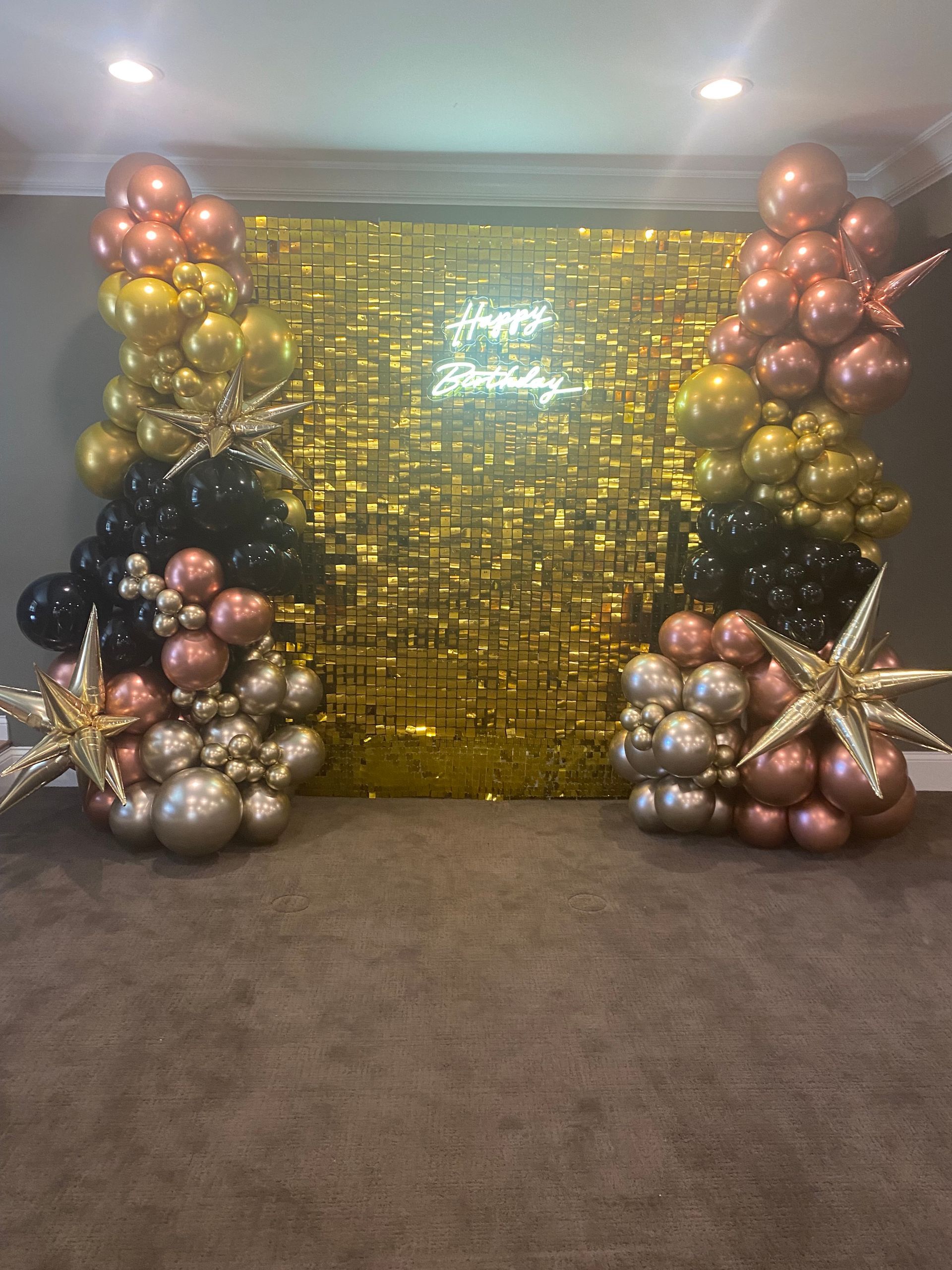 Gold sequin backdrop with pink and gold balloon clusters and star decor on a carpeted stage