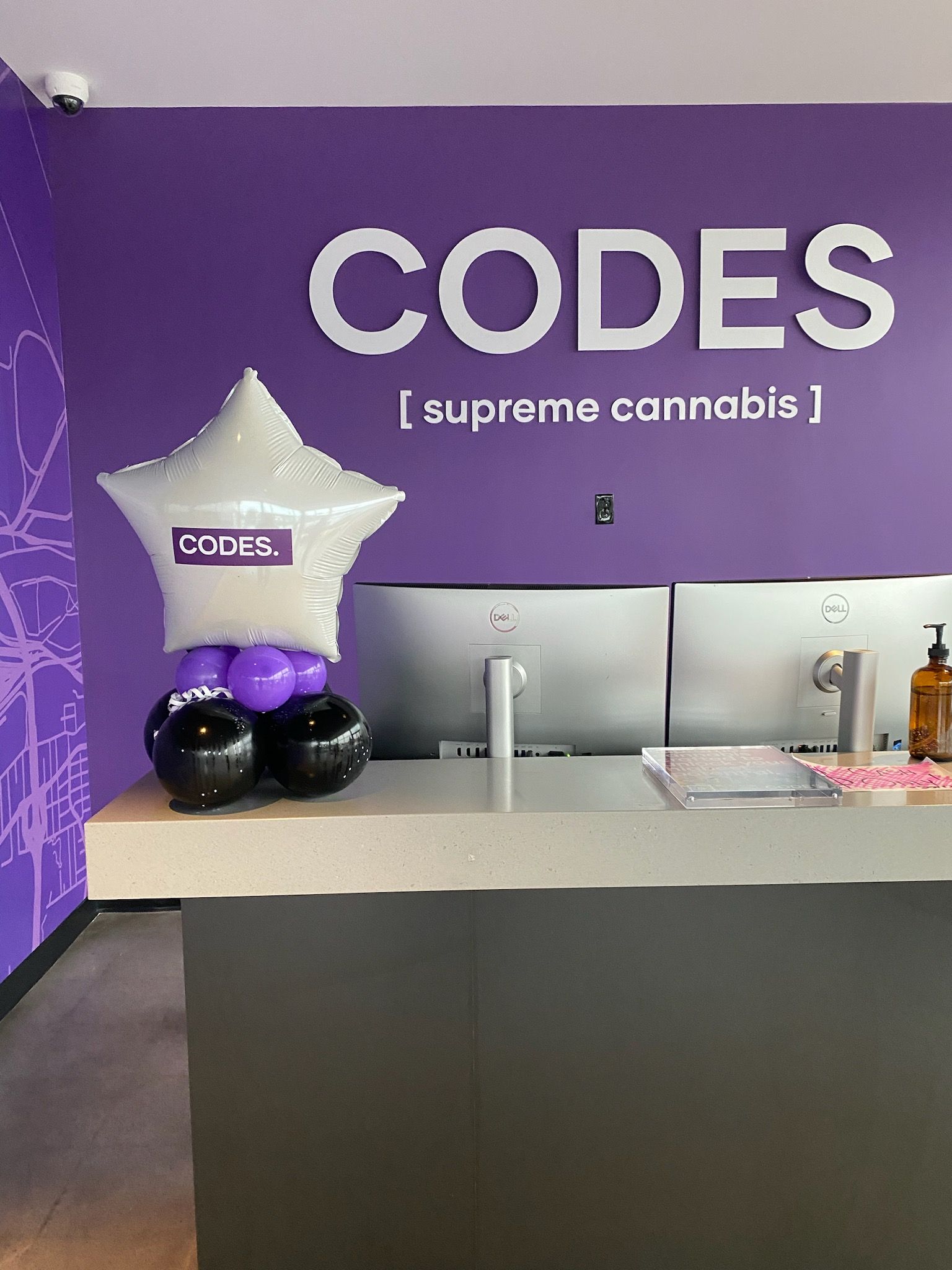 Purple CODES dispensary counter with branded wall, star balloon, and cannabis display items