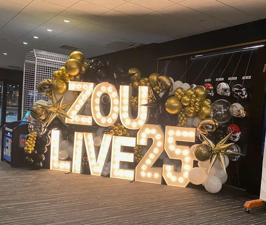 Gold balloon display reading “ZOU LIVE25” in a decorated indoor event space