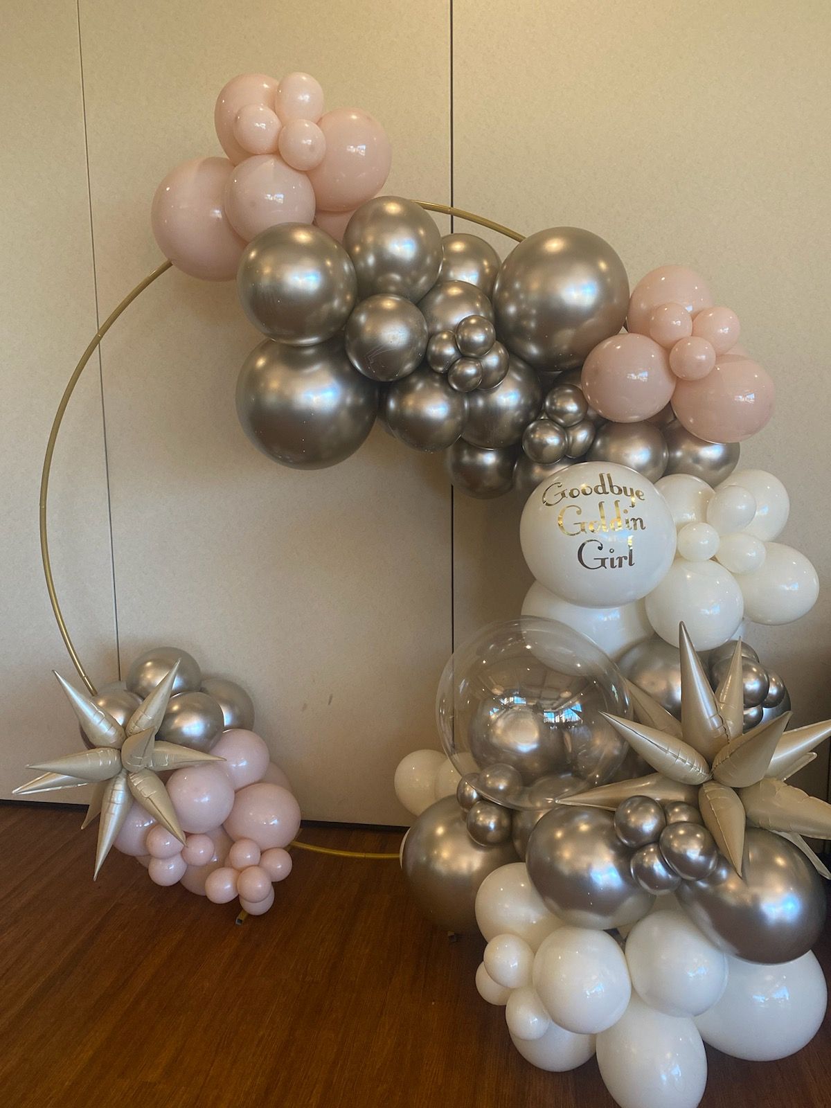 Neutral balloon garland display in metallic silver, blush pink, and white with floral accents, indoors on wood floor