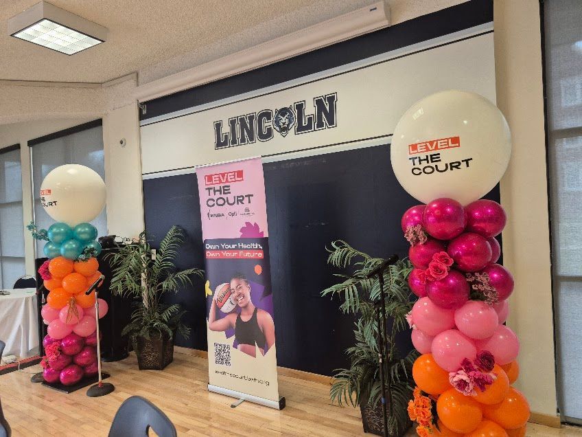 Balloon columns flank a “Lincoln” school entrance with a TEAM Court banner and poster displays.