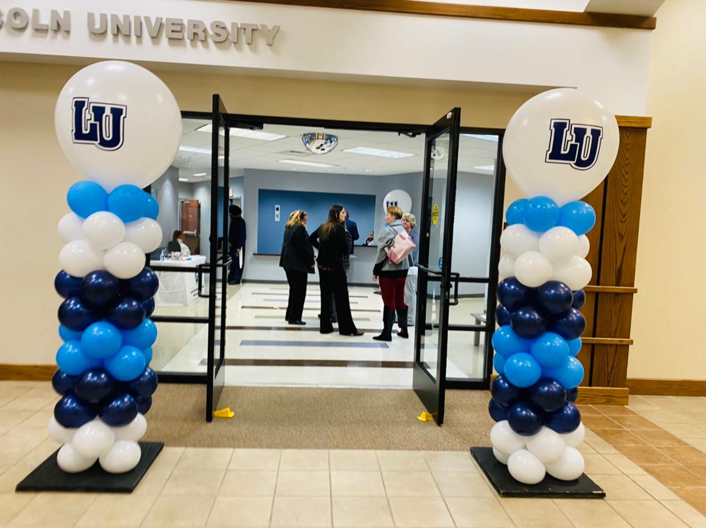 Blue and white balloon columns framing a university entrance with people inside