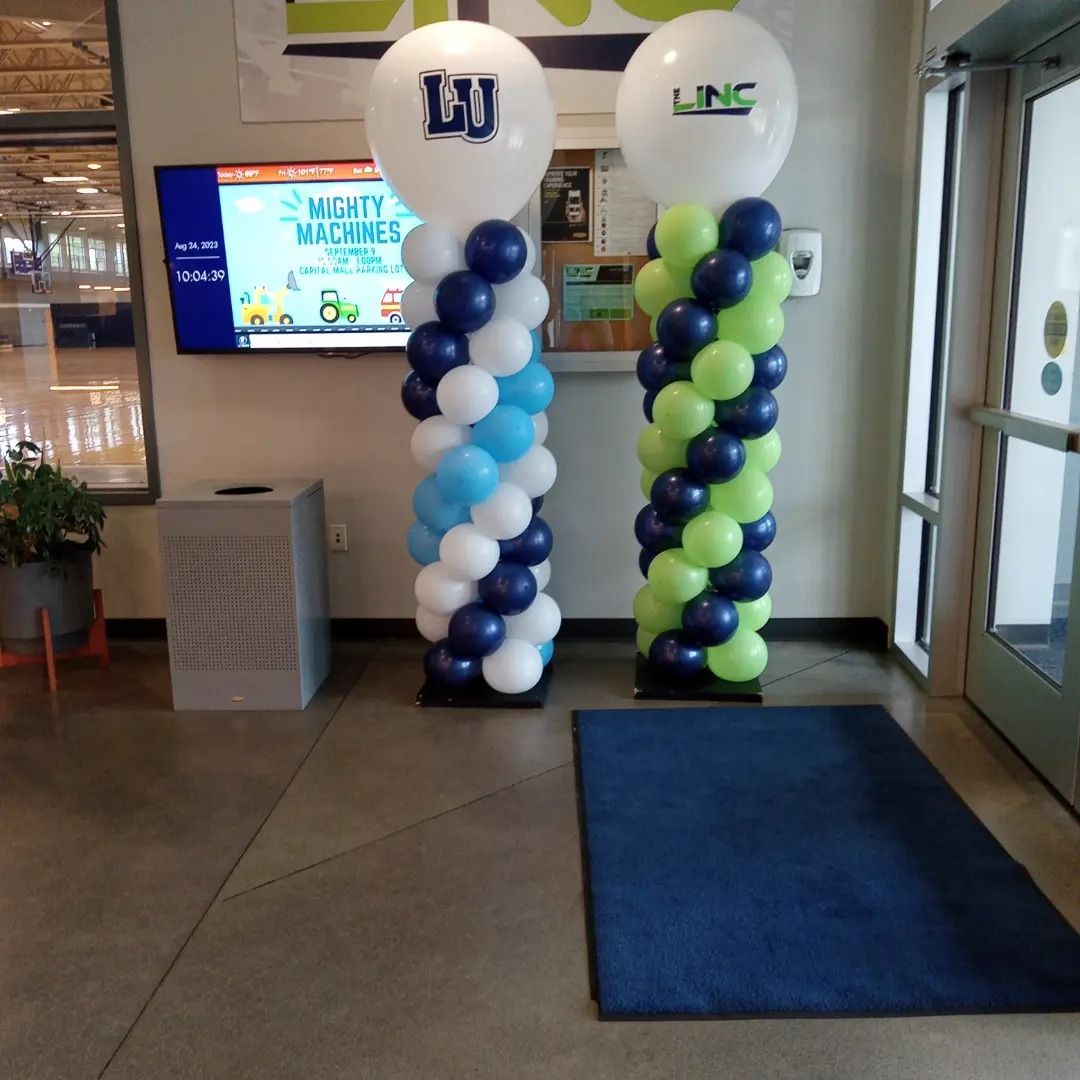 Decorated lobby entrance with blue and green balloon columns, a blue rug, and glass doors.