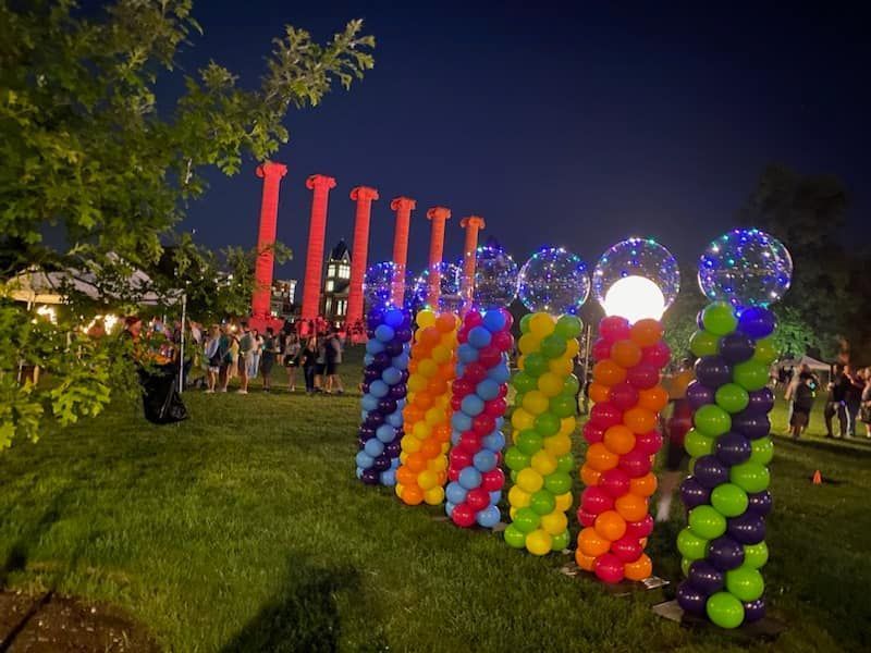 Outdoor nighttime event with colorful balloon columns and glowing spheres on a grassy lawn
