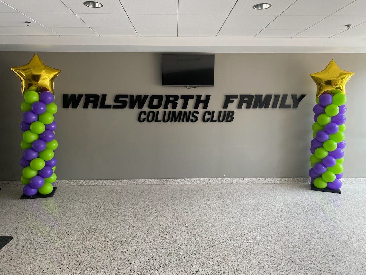 Walsworth Family Columns Club sign flanked by purple, green, and gold balloon columns with star tops
