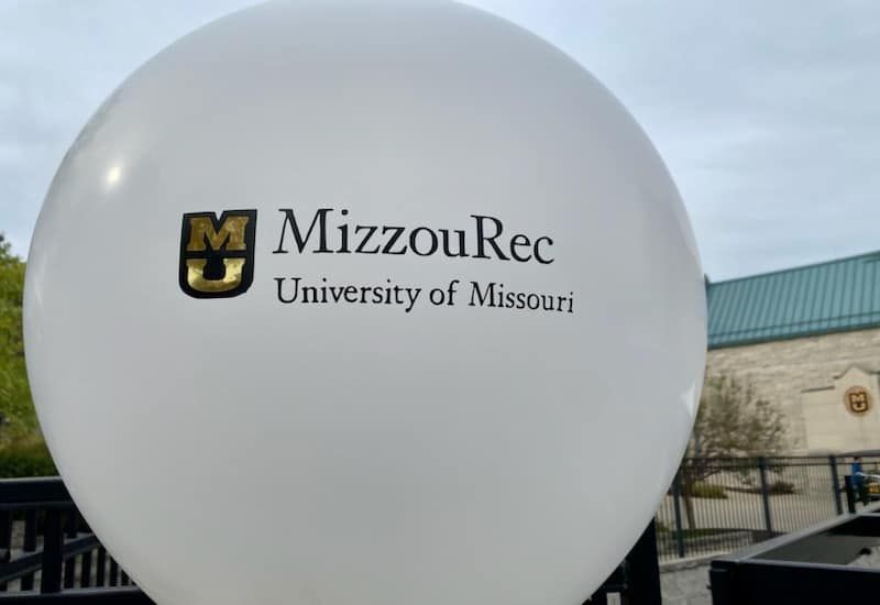 Large white balloon with MizzouRec and University of Missouri logo outdoors on campus