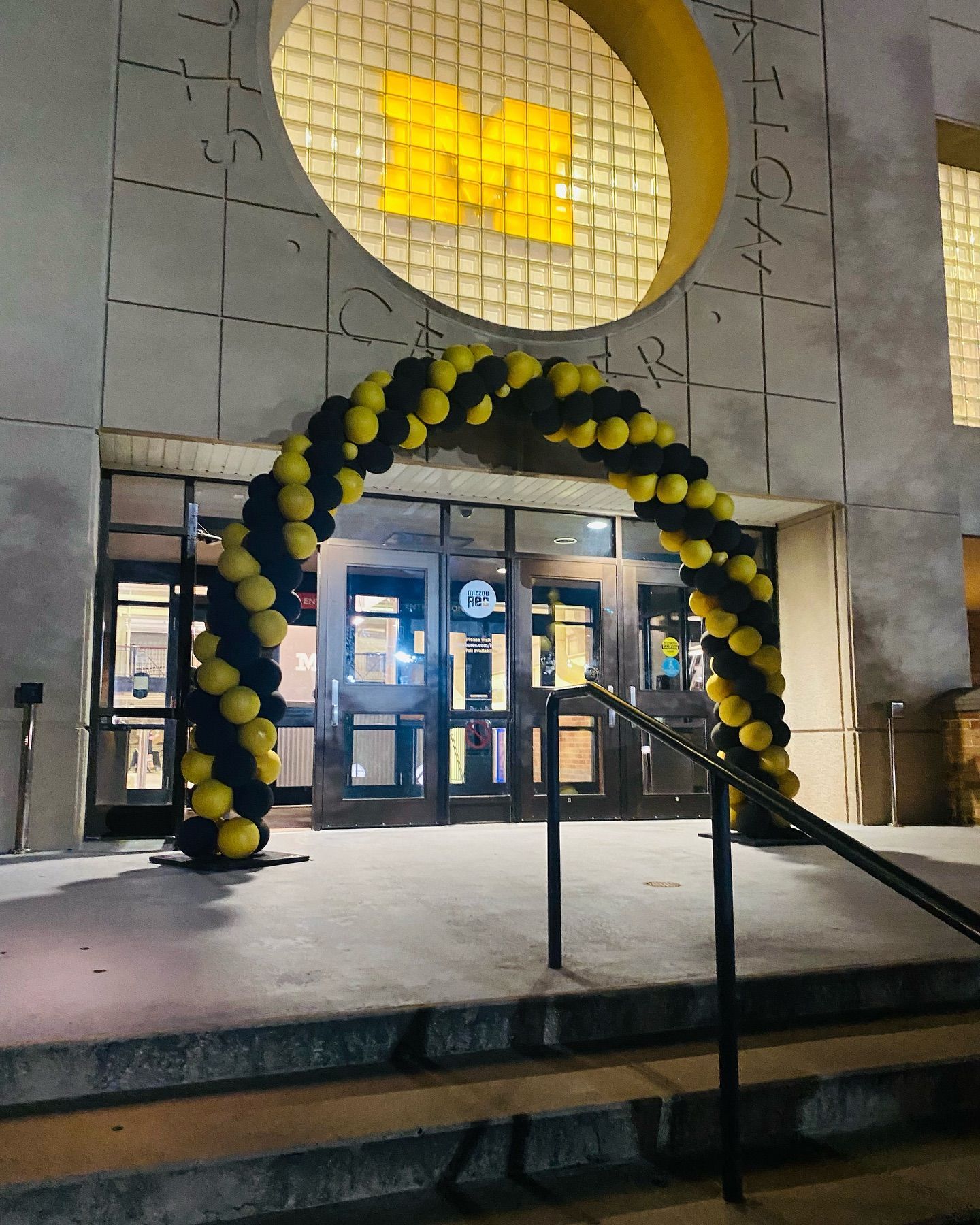Yellow and black balloon arch at a building entrance at night