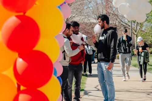 People chatting on a sunny sidewalk near a colorful balloon display