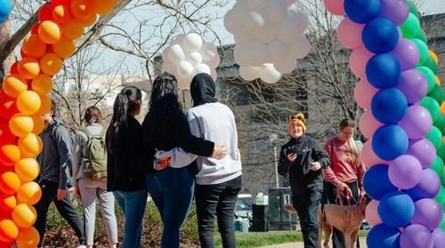 People standing under colorful balloon arches at an outdoor event with white balloons overhead