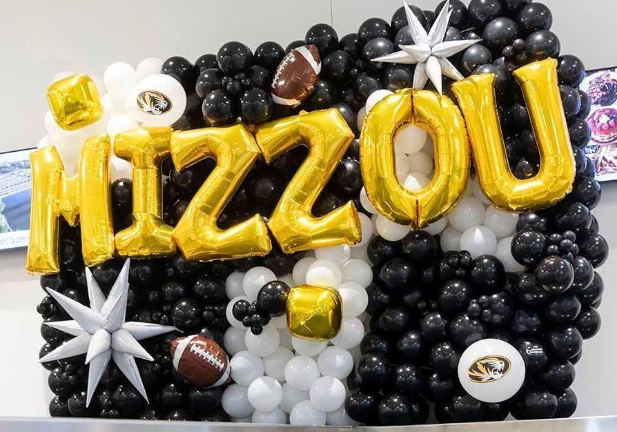 Gold “MIZZOU” letters on black-and-white football-themed balloons and decorations