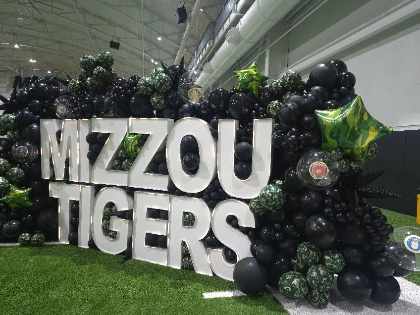 Mizzou Tigers sign in white letters surrounded by black balloons and green star balloons indoors
