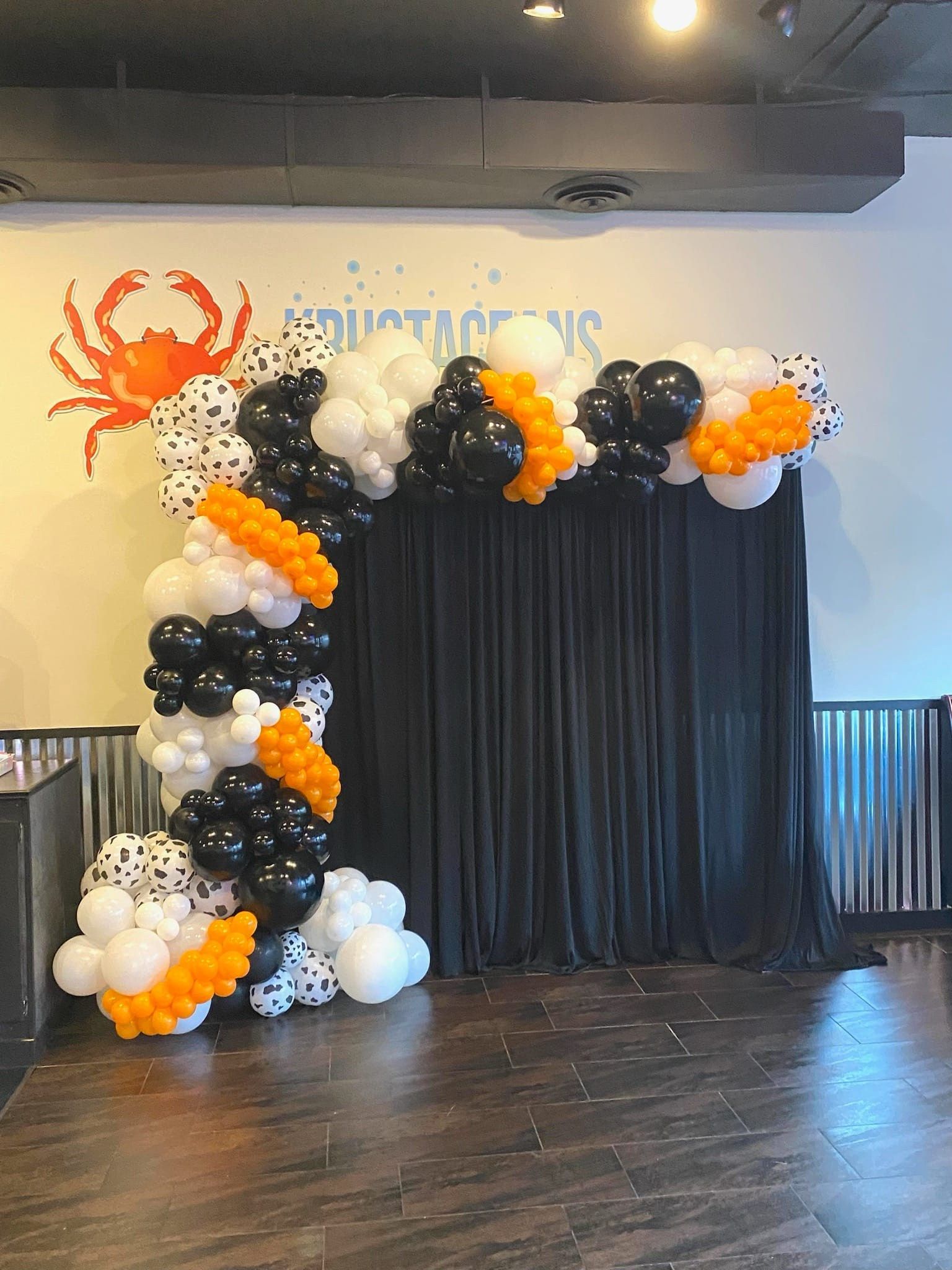 Black, white, and orange balloon arch framing a black curtain stage backdrop indoors