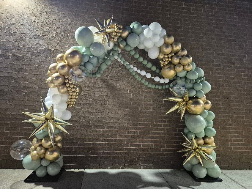 Balloon arch in white, gold, and sage green against a brick wall