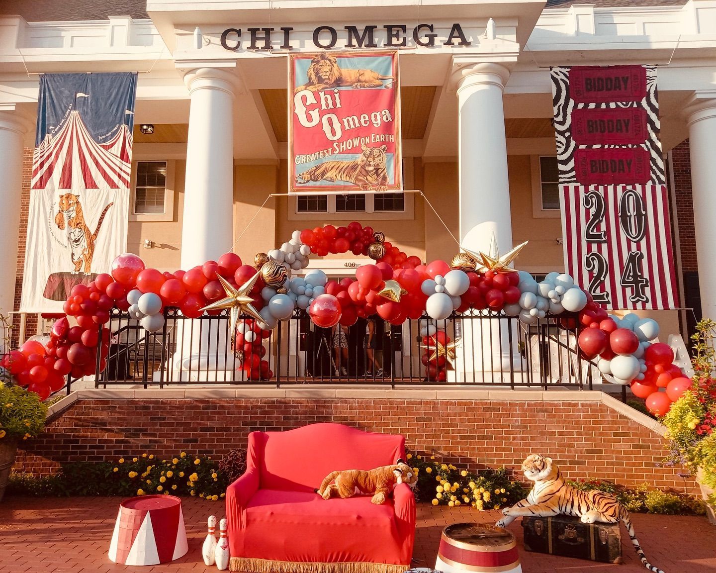 Red, white, and blue Chi Omega house decorated with balloons, banners, and patriotic lawn decor.