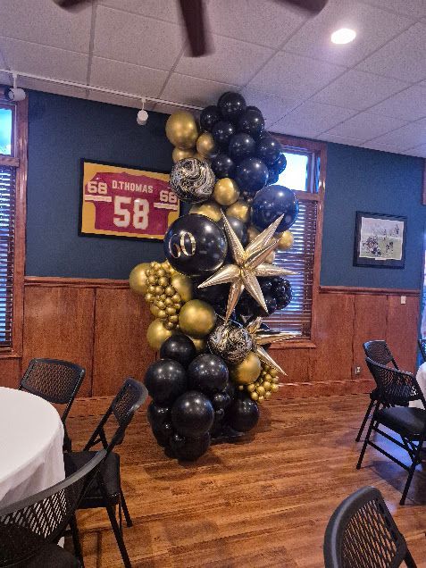 Black, gold, and silver balloon column beside a red “56” sign in a restaurant dining room