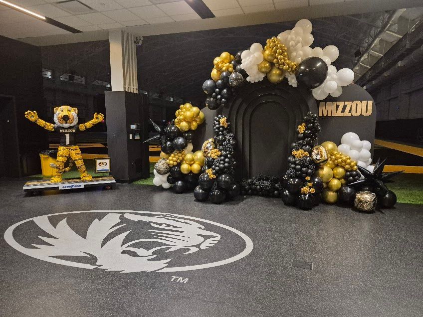 Gold, black, and white balloon display with Missouri Tigers signage and a tiger mascot backdrop in an indoor lobby