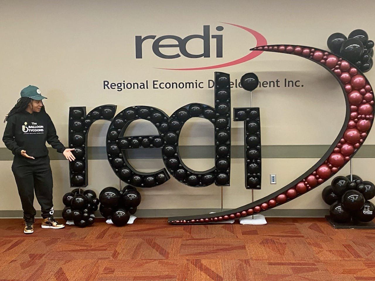 Person standing beside large black and pink “redi” balloon display at a Regional Economic Development event.