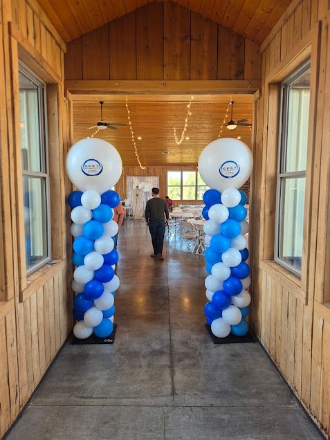 Blue-and-white balloon columns framing a wooden hall entrance with a person walking inside