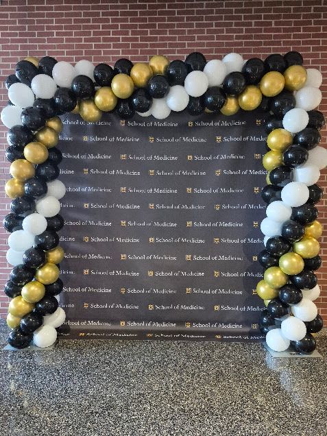 Black, gold, and white balloon arch framing a memorial sign on a floor