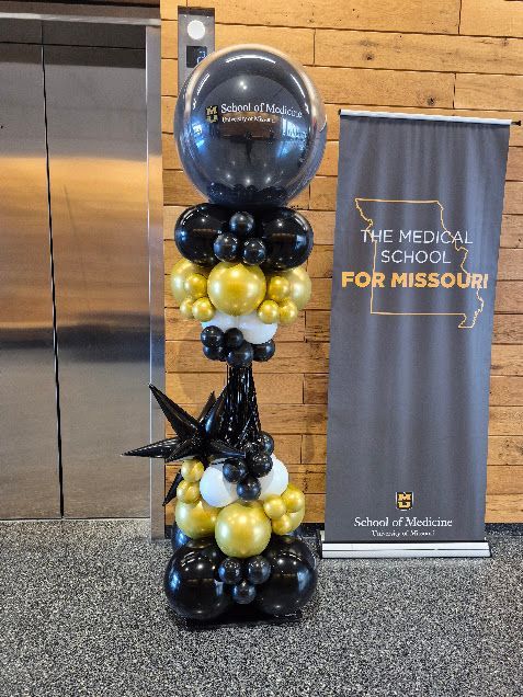 Balloon column in black, gold, and white beside a Missouri School banner indoors
