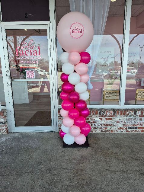 Pink and white balloon column beside a storefront entrance with a round pink balloon topper
