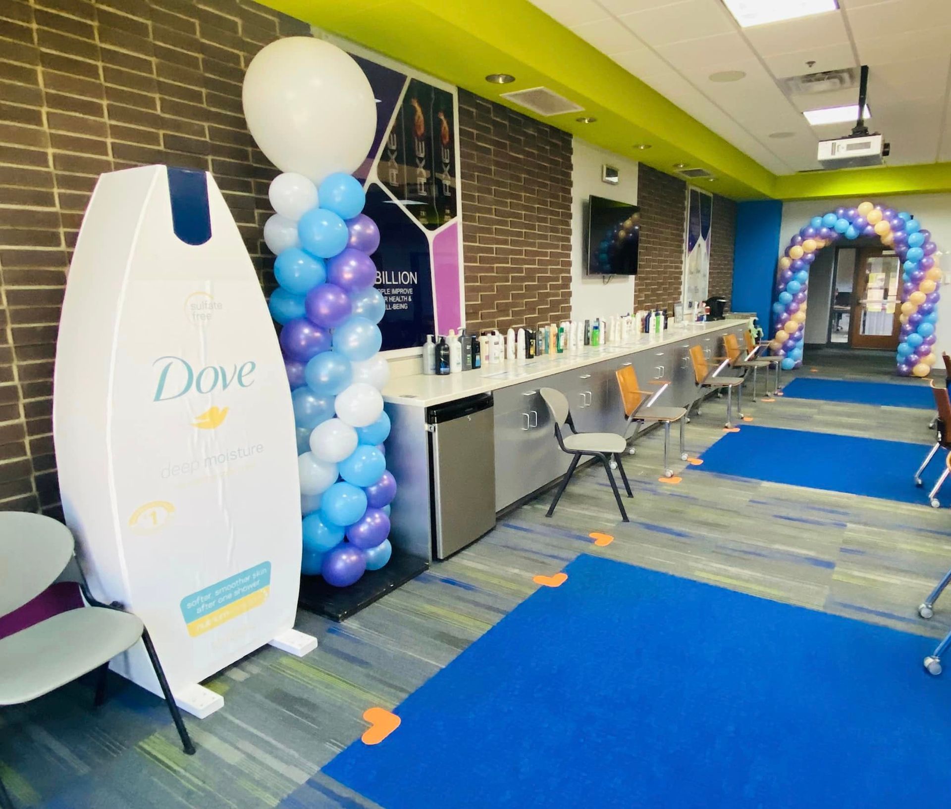 Dove product display in a colorful retail event space with blue carpet and balloon arch entrance