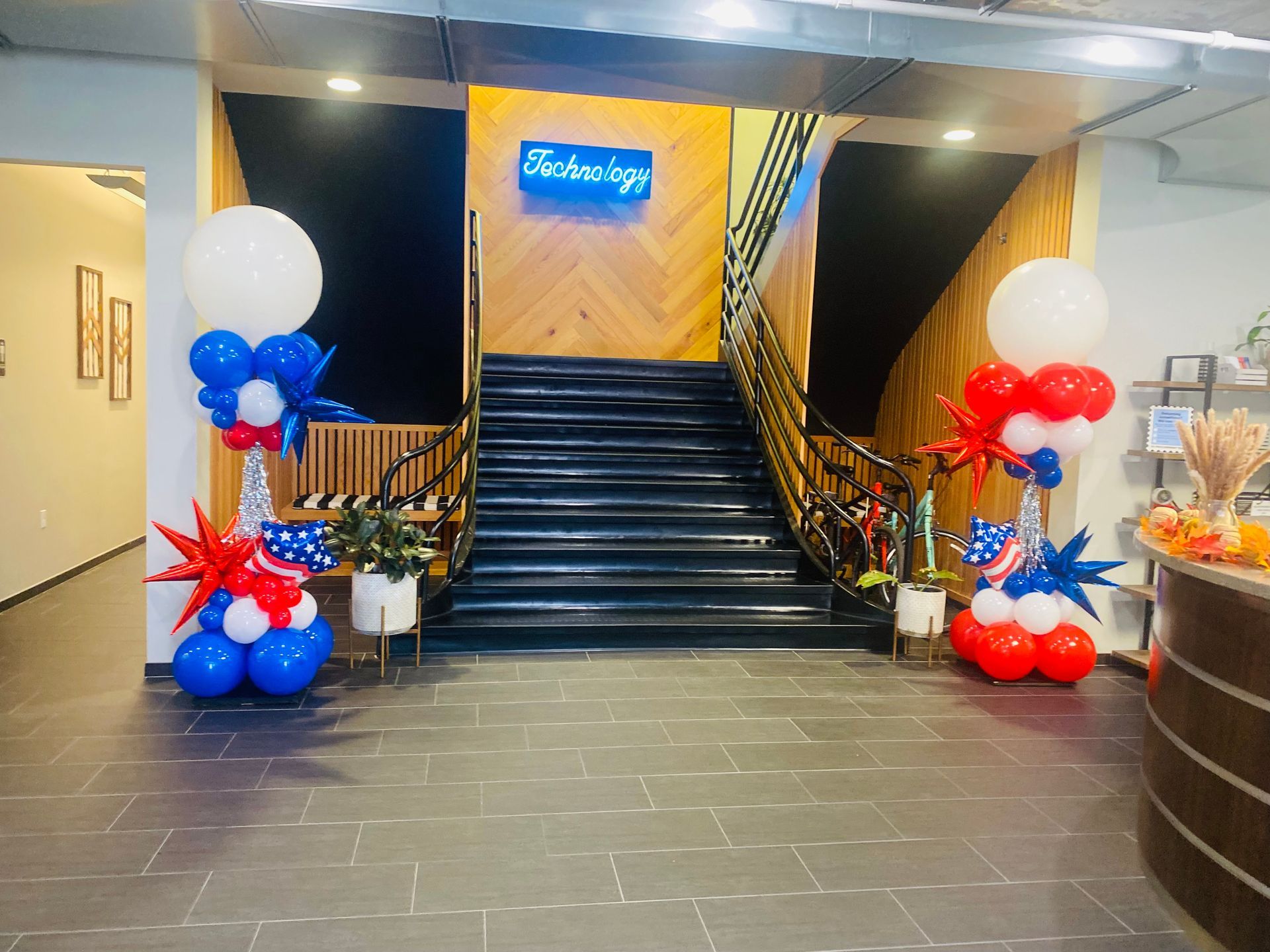 Decorated lobby staircase with red, white, and blue balloons and a glowing sign above the stairs