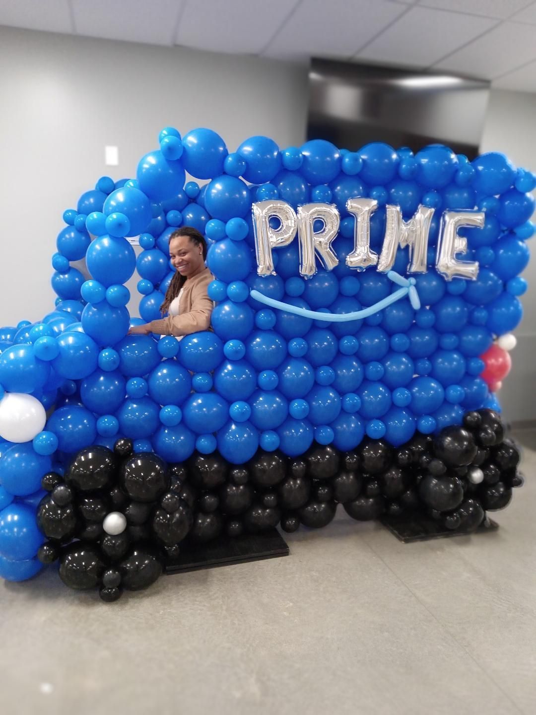 Blue balloon display shaped like a car with “PRIME” and a child peeking through a window