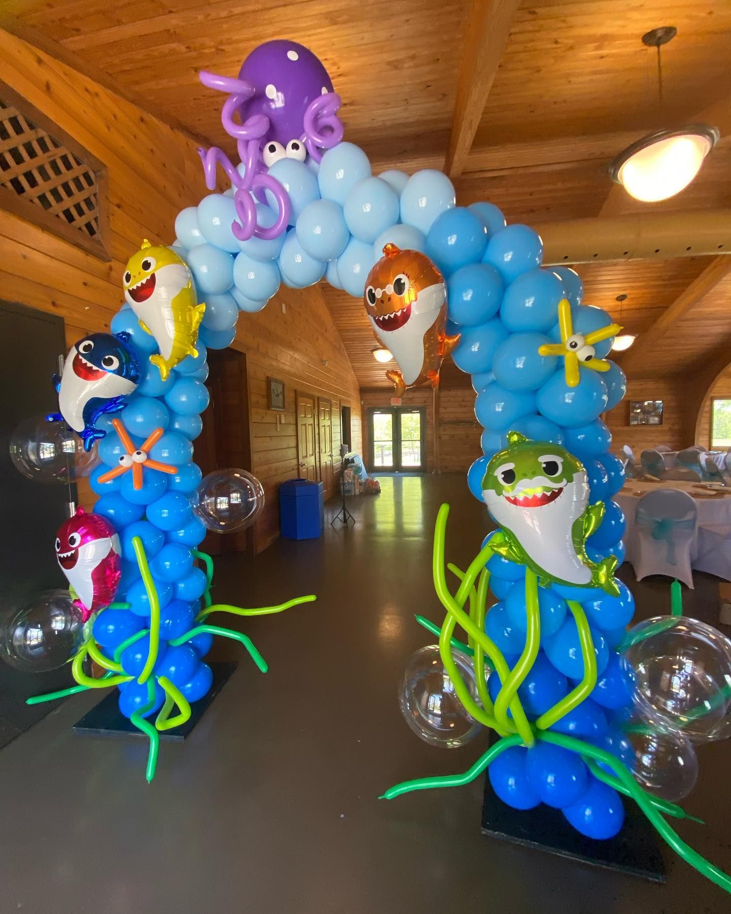 Colorful balloon sea creatures arching over a wooden hall entrance, with blue, green, and purple balloons.