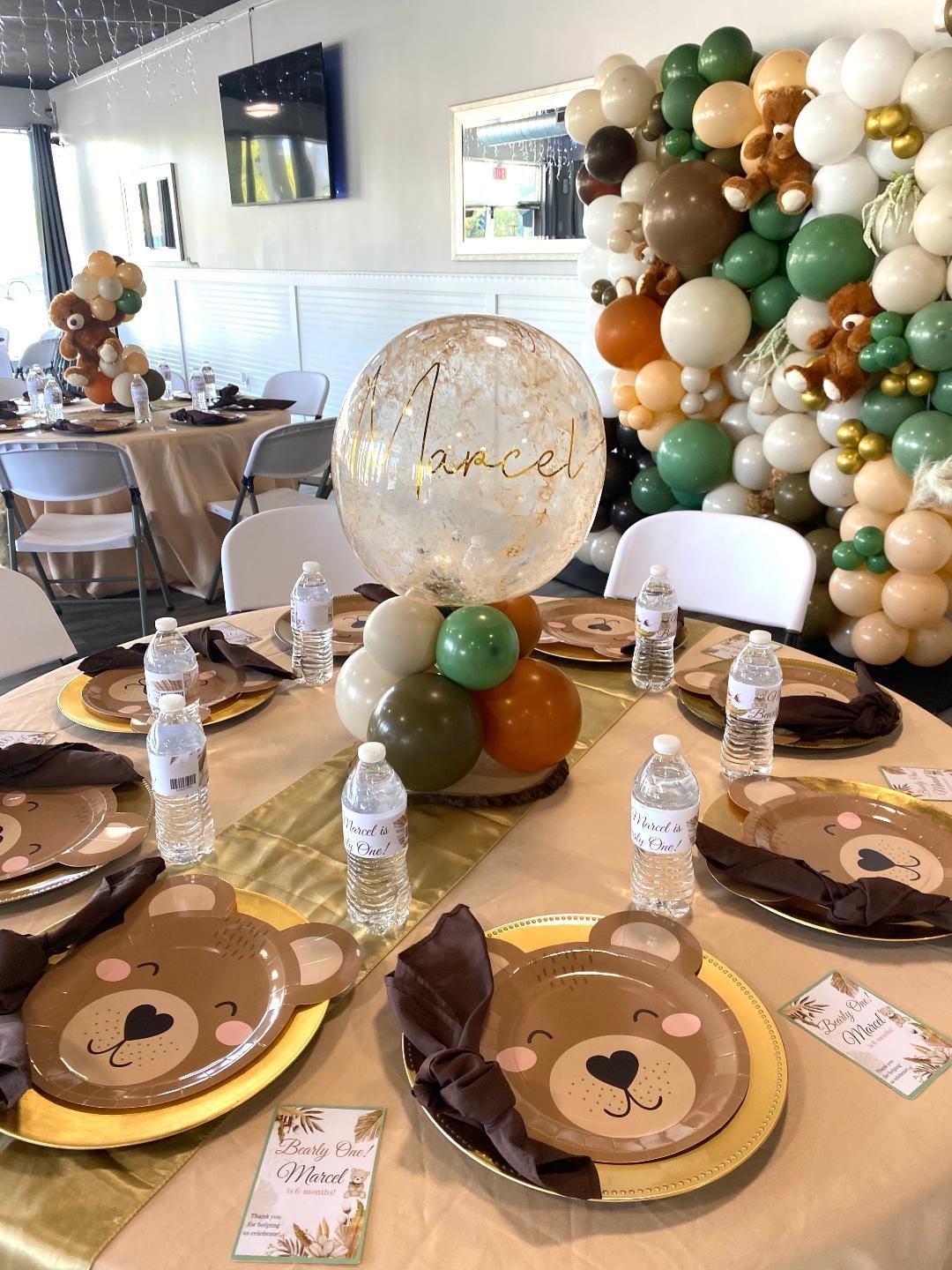 Balloon-decorated table with bear plates, water bottles, and a clear centerpiece at a party setup
