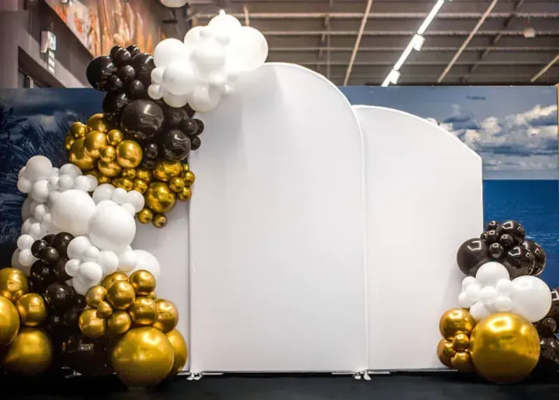 White photo booth surrounded by black, white, and gold balloon clusters in an indoor venue