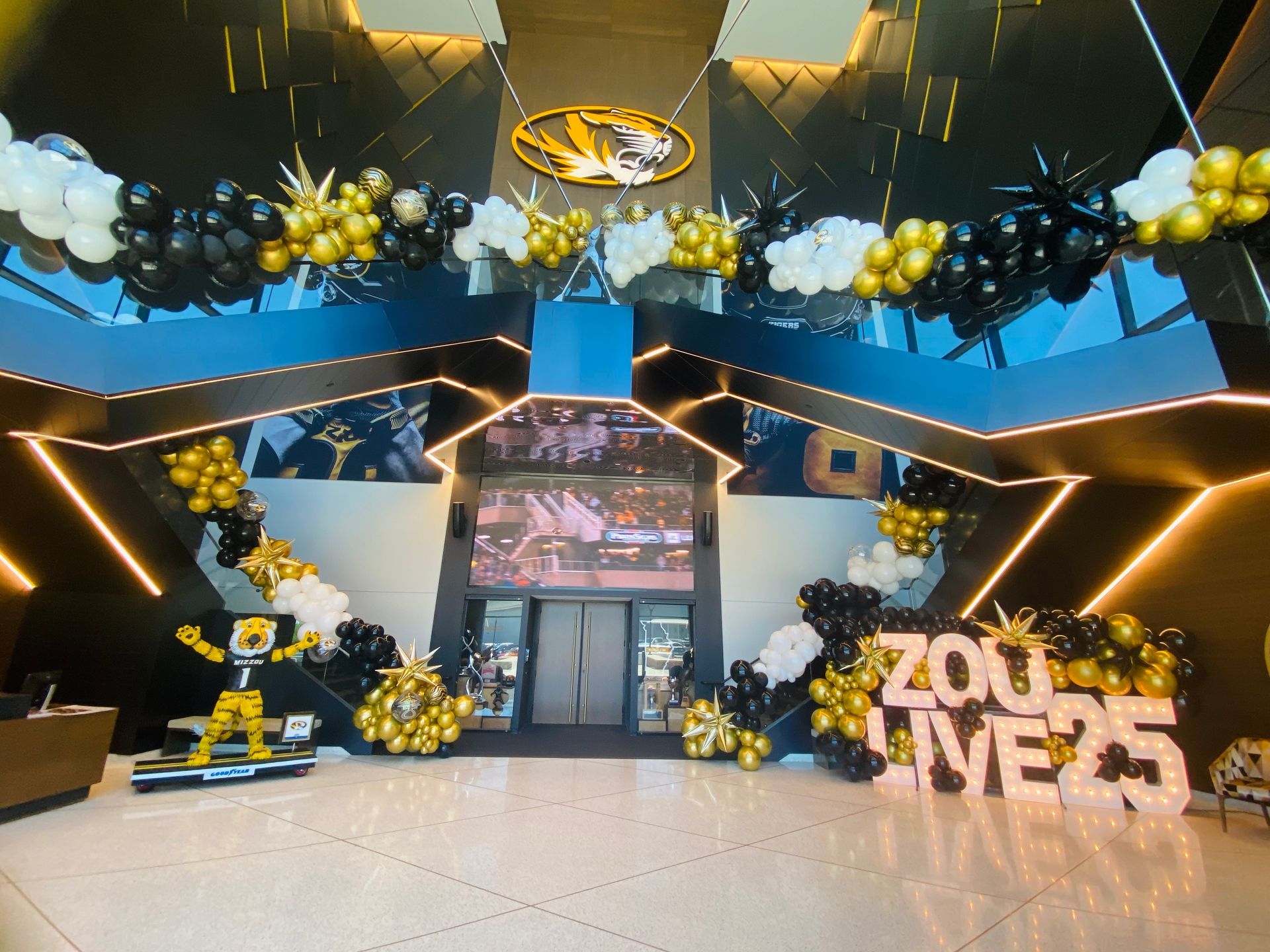 Decorated event entrance with black, gold, and blue balloons and a large “2025” sign