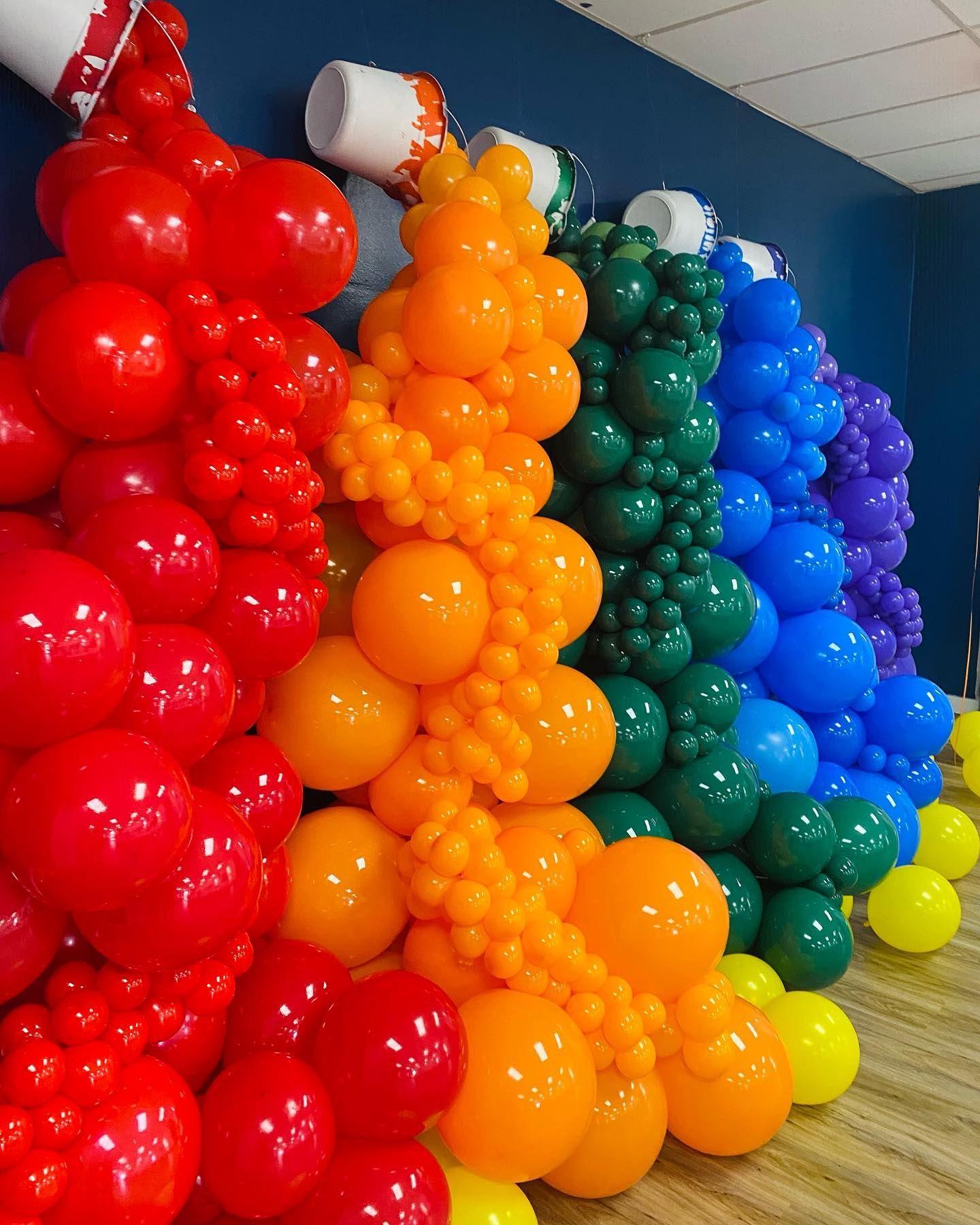 Colorful balloon columns arranged in rainbow order against a blue wall.