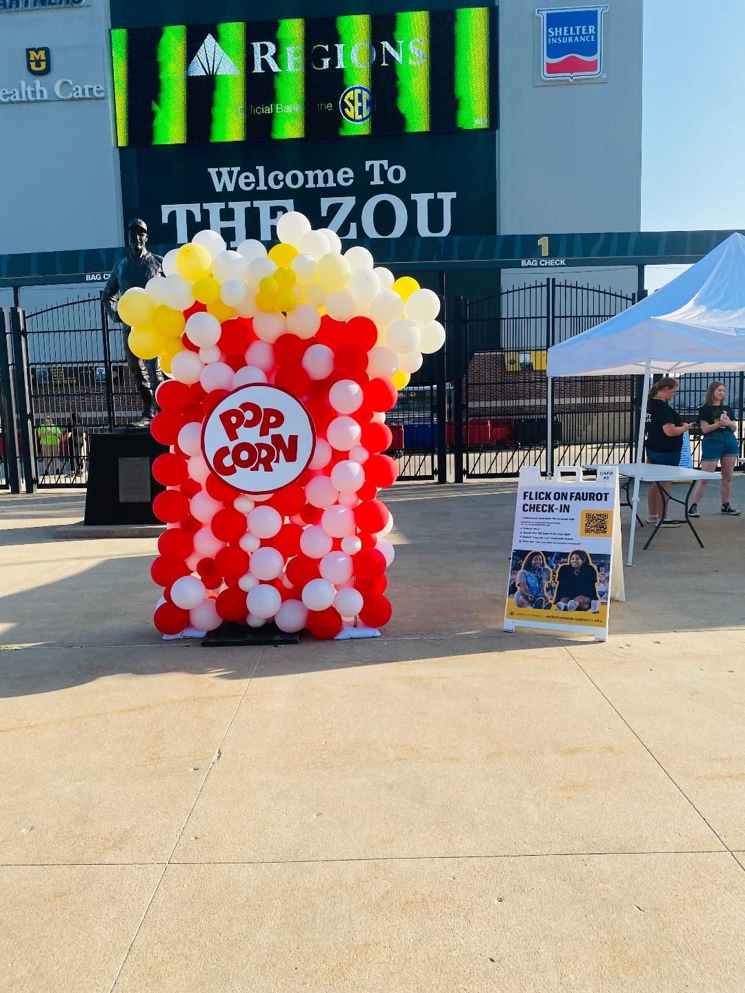 Outdoor popcorn stand made of red and white balloons under a “Welcome to the Zoo” sign