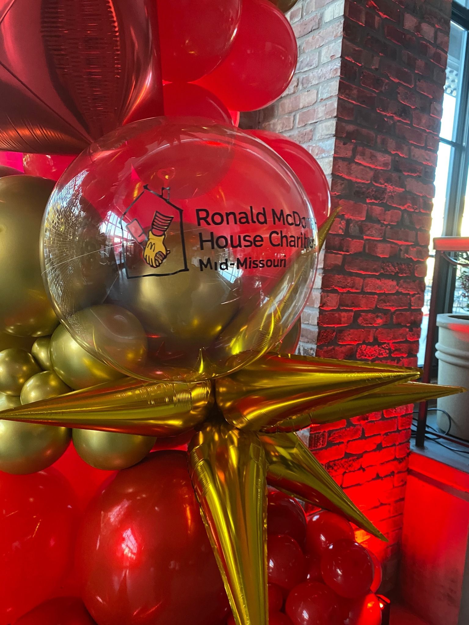 Red and gold balloon display with Ronald McDonald House Charities logo on a mirrored balloon.