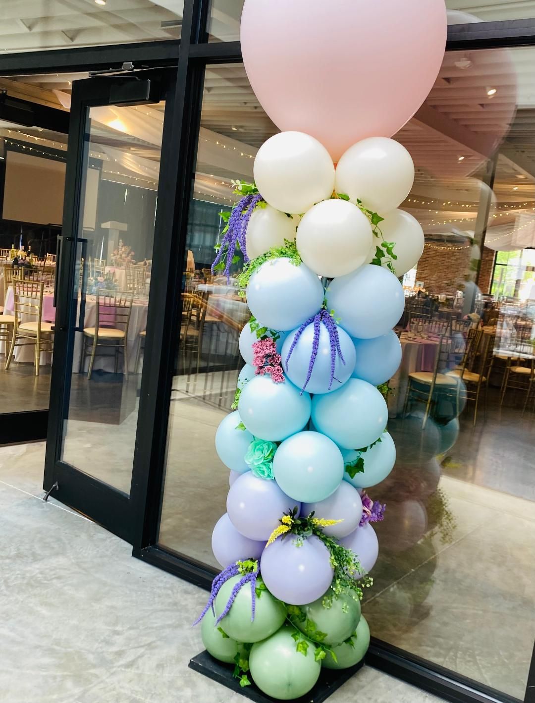 Pastel balloon column by a glass storefront, topped with a large pink balloon