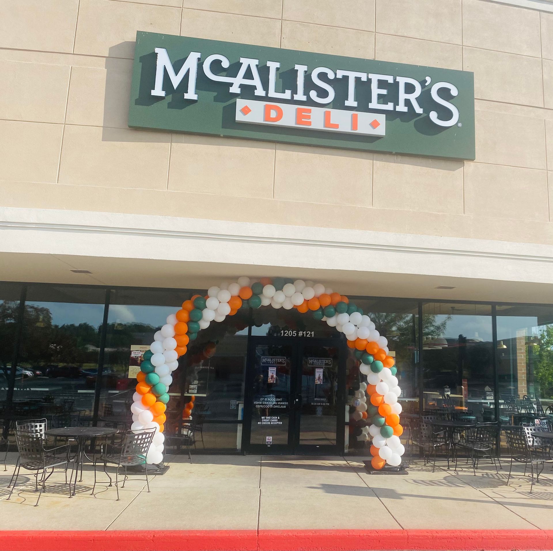 McAlister’s Deli storefront with a white, green, and orange balloon arch at the entrance