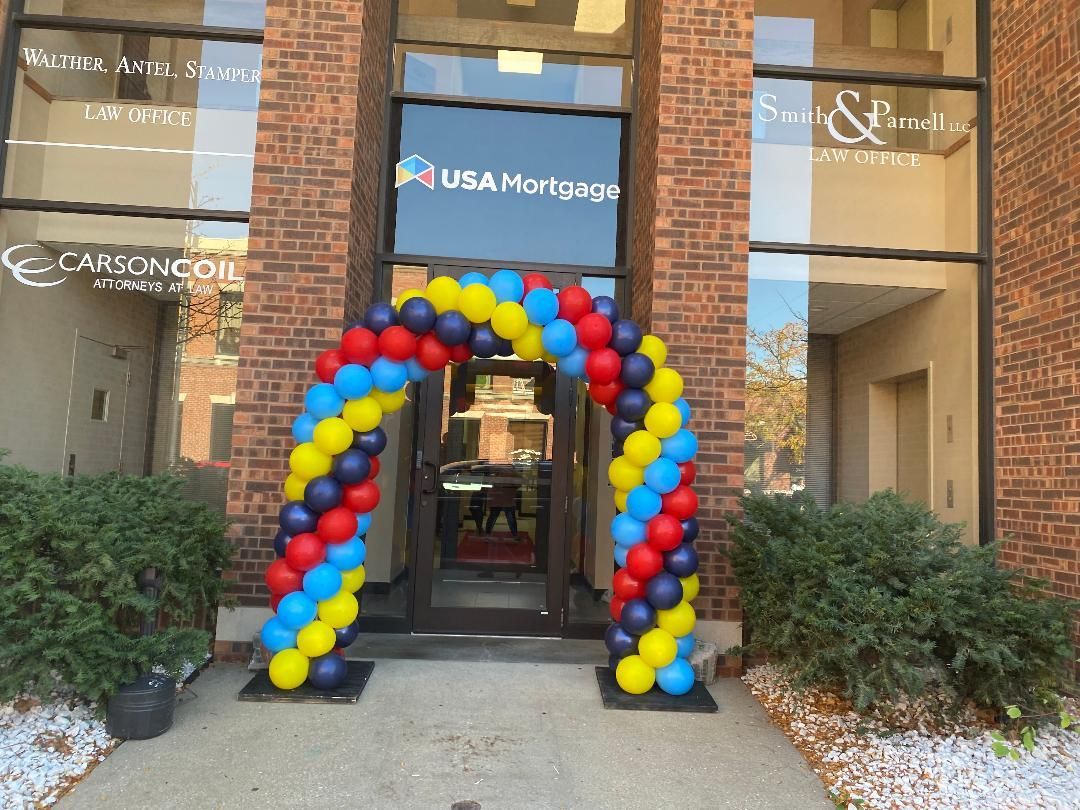 Balloon arch in red, yellow, and blue at the entrance of a storefront building
