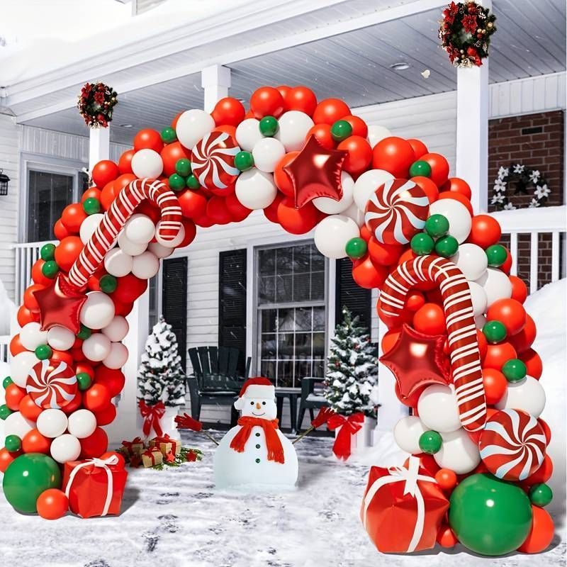 Festive Christmas balloon arch with red, green, and white decorations around a snowy front porch and snowman