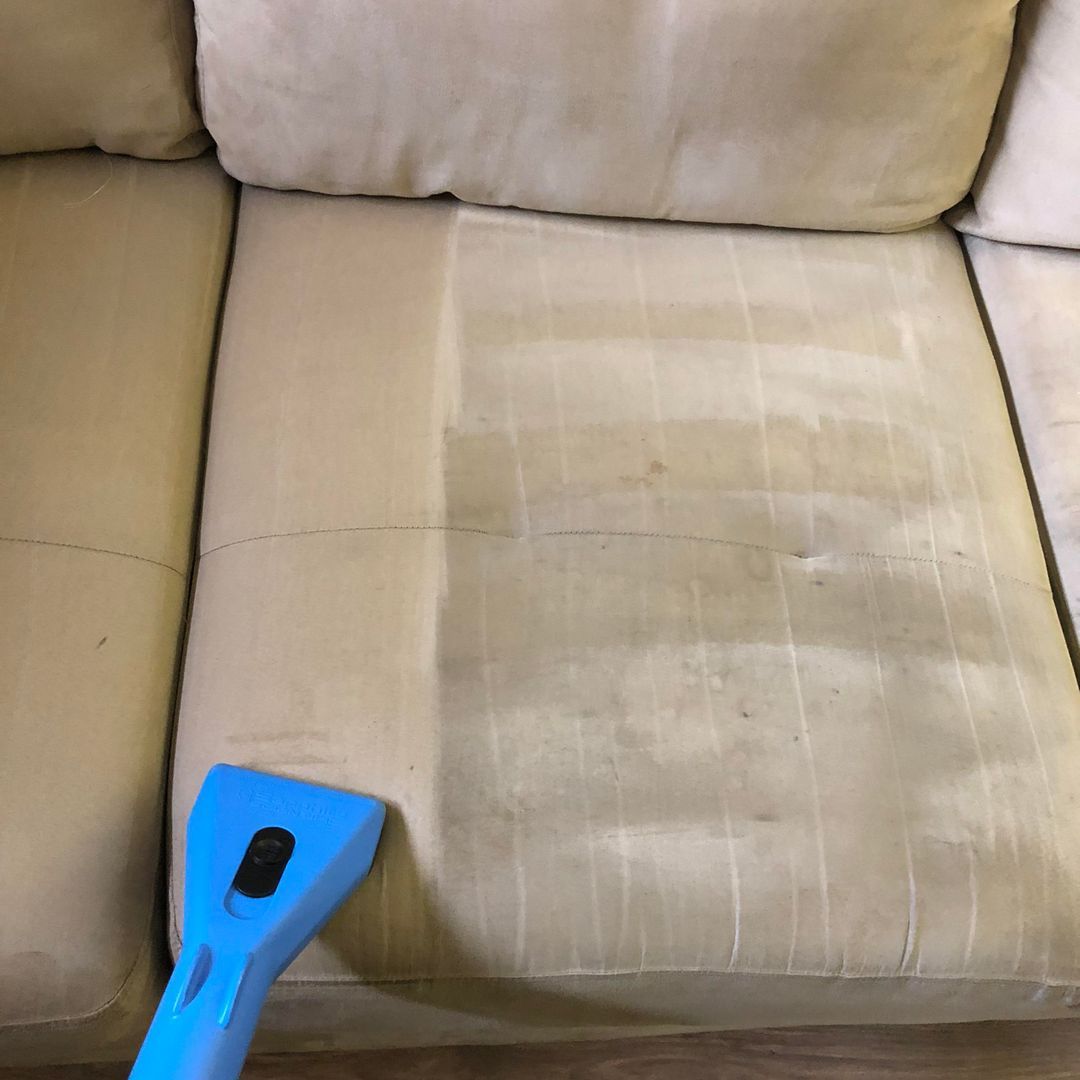 Beige couch cushion with a large stain being cleaned with a blue upholstery tool