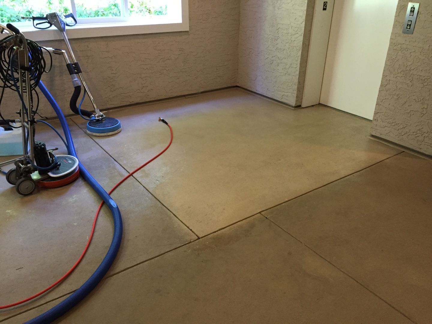 Concrete floor with a window, cleaning equipment, and hoses in a room under construction.