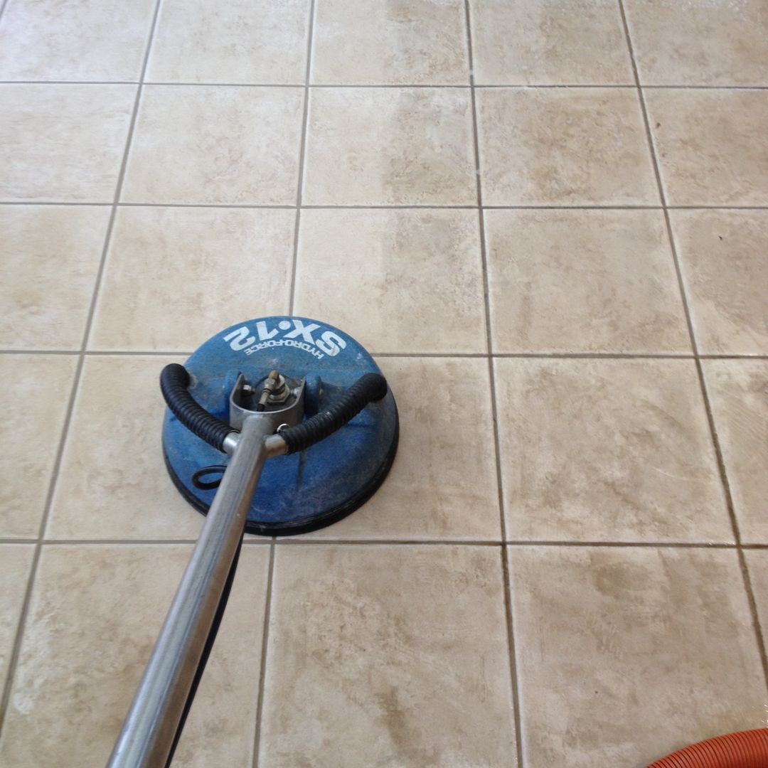 A blue floor scrubber cleaning beige tiled floor, viewed from above.